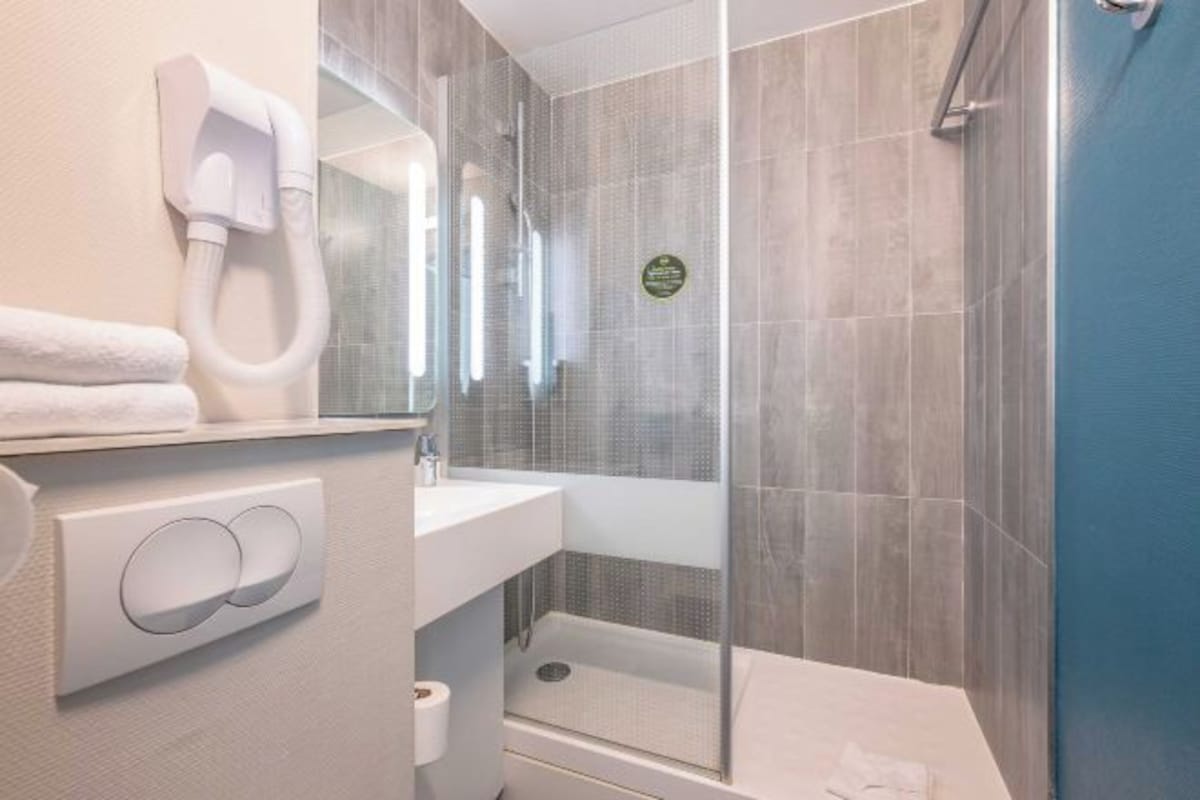 A modern bathroom with a glass-enclosed shower, a white sink, and a towel dispenser.