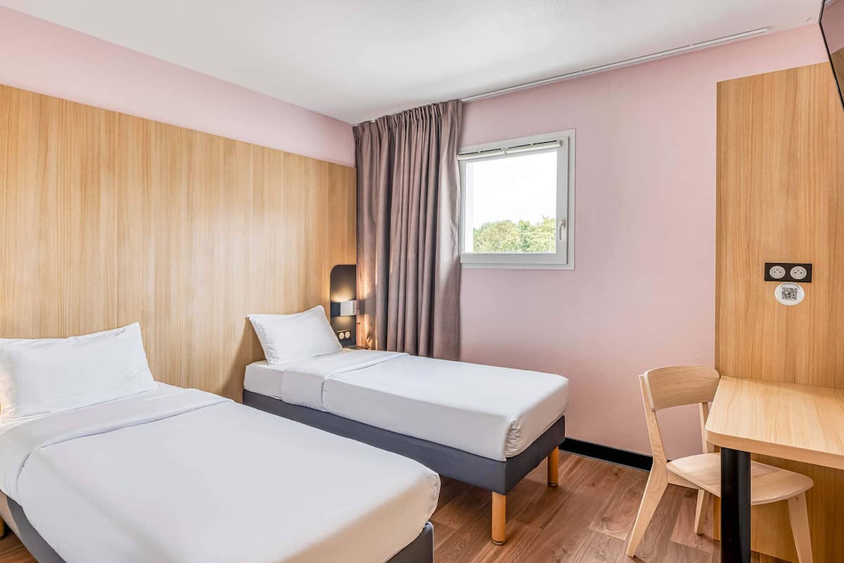 A hotel room with two beds, a desk, and a window with curtains.