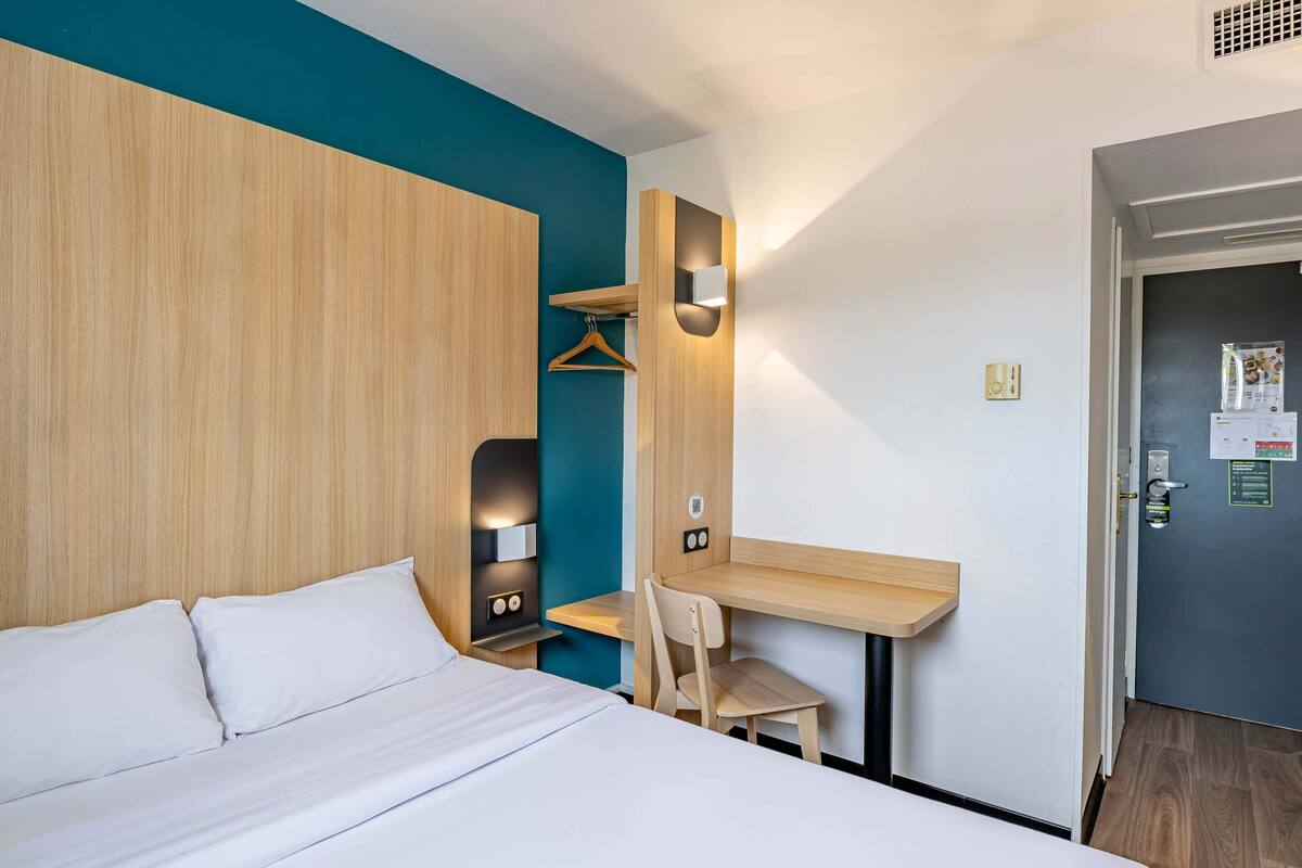 A hotel room with a bed, a desk, a chair, and a wardrobe.