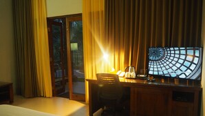A hotel room with a bed, a desk with a computer, a chair, and a large window with curtains. - The Gecho Inn Country (Jepara)