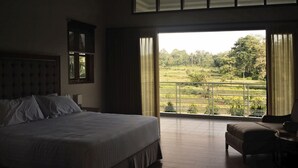 A bedroom with a large bed, a chair, and a balcony with a view of greenery. - The Gecho Inn Country (Jepara)