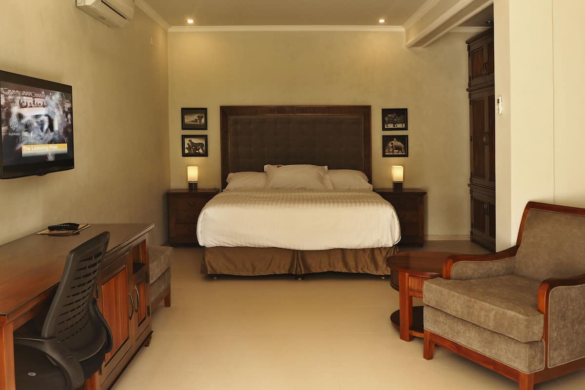 A hotel room with a large bed, two bedside tables with lamps, a desk with a chair, a TV mounted on the wall, and a wardrobe.
