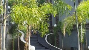 A curved staircase surrounded by tall trees and a building with a stone facade. - The Gecho Inn Country (Jepara)
