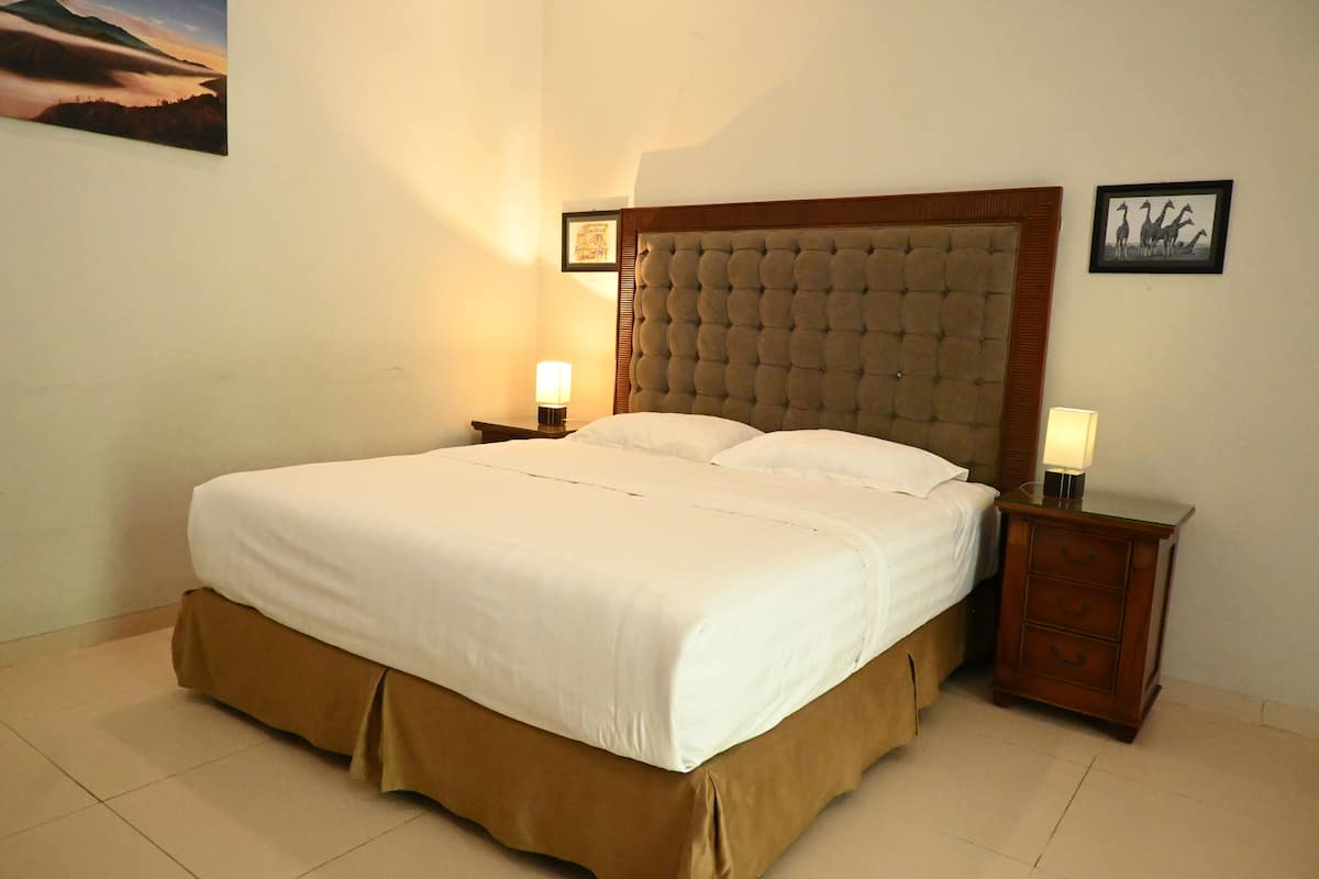 A neatly made bed with a brown skirt, two bedside tables with lamps, and framed pictures on the walls.
