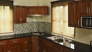 A kitchen with wooden cabinets, a black countertop, a stainless steel sink, and a tiled backsplash. - The Gecho Inn Country (Jepara)