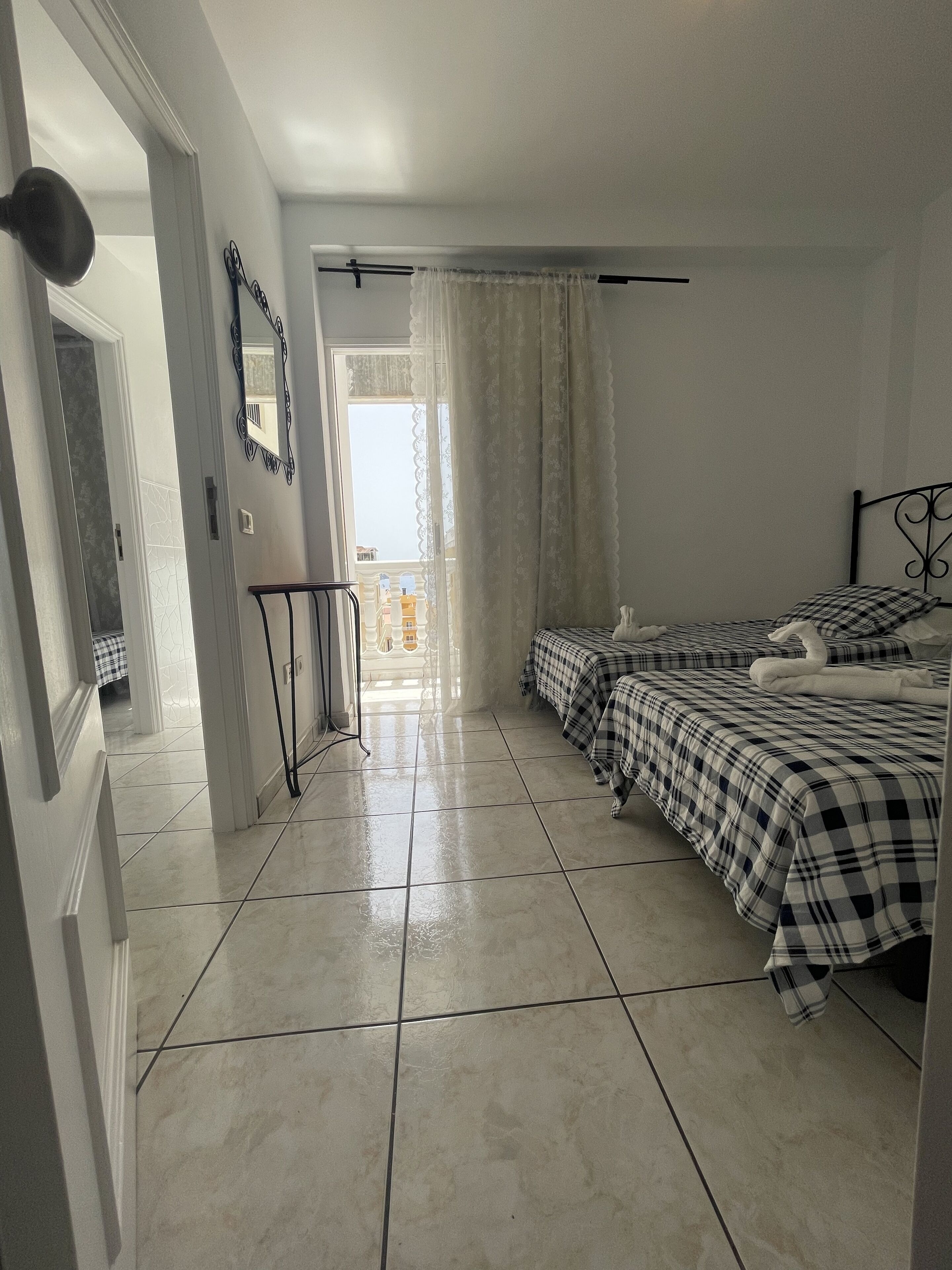 A bedroom with two beds, a door, a mirror, and a view of the outside.