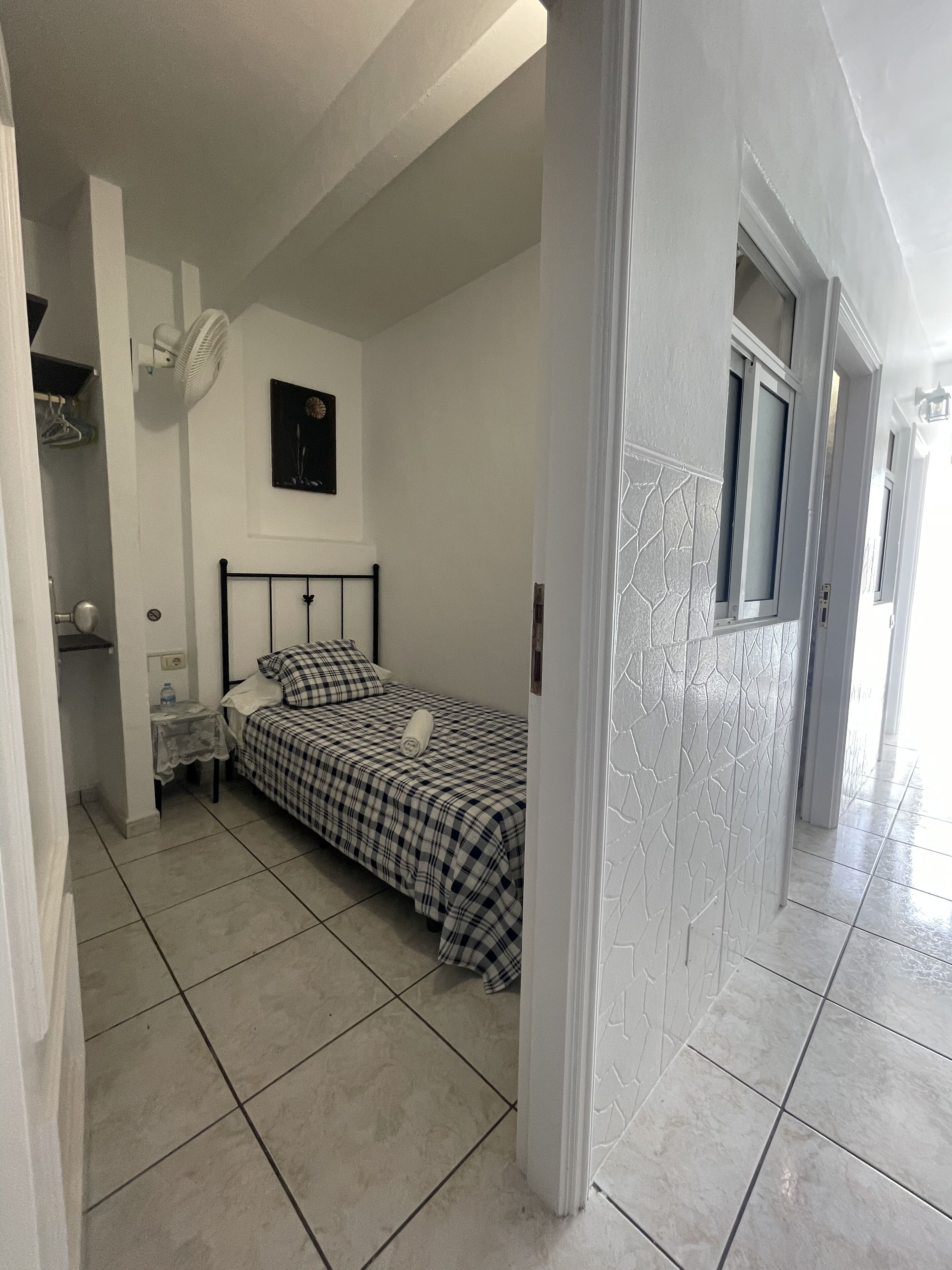 A bedroom with a bed, a nightstand, a wall clock, and a door leading to another room.