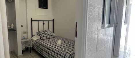 A bedroom with a bed, a nightstand, a wall clock, and a door leading to another room.