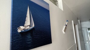 Um corredor com um quadro fixado na parede retratando um veleiro na água, uma parede branca com textura e uma porta com padrão geométrico.