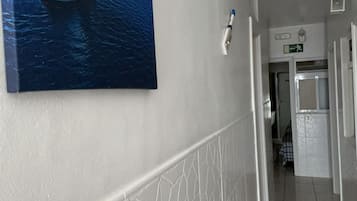 A hallway with a tiled floor, a white wall with a decorative pattern, and a painting of a sailboat on the wall.