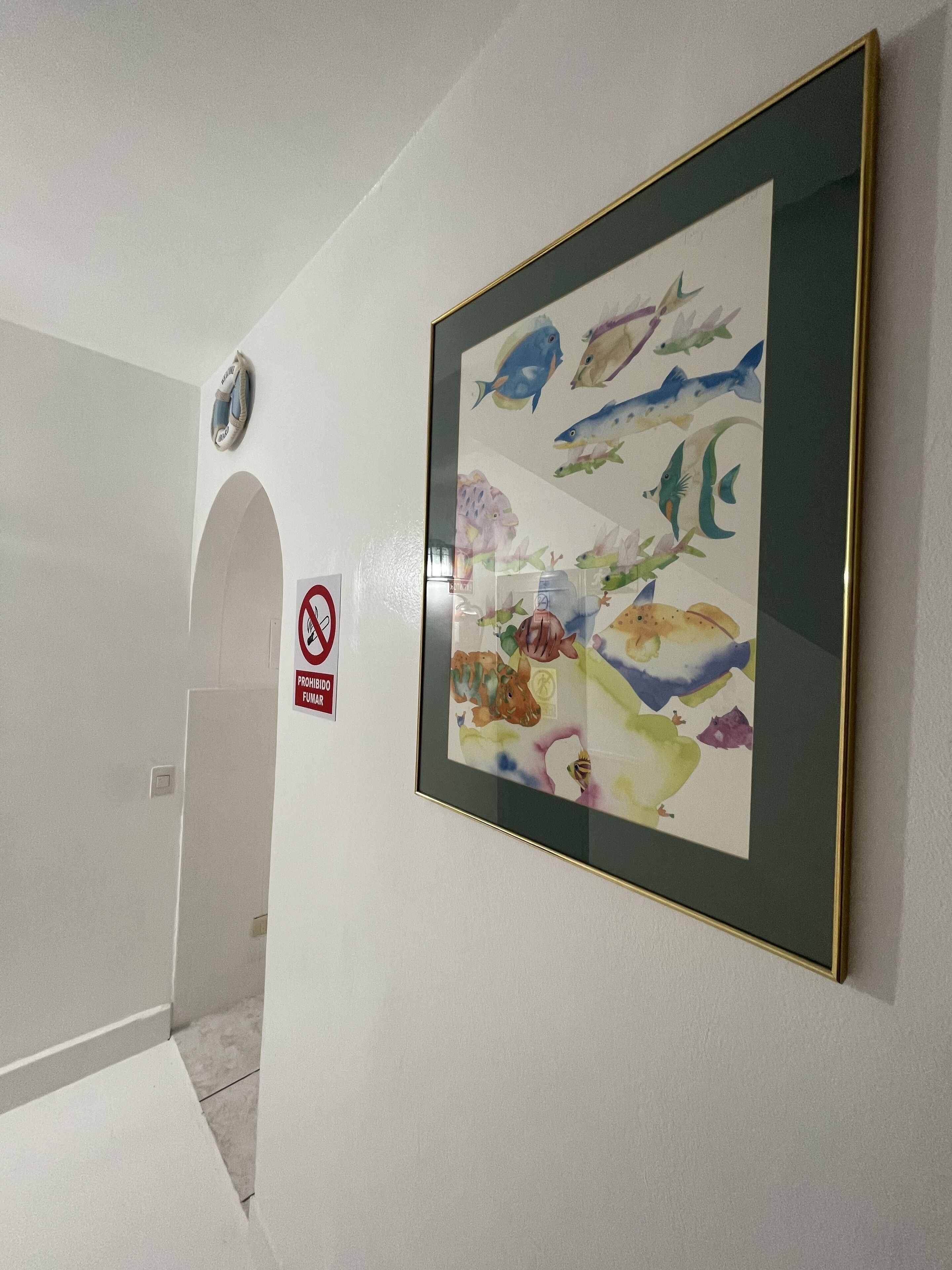 A hallway with a framed artwork of fish on the wall, a no smoking sign, and a smoke detector.