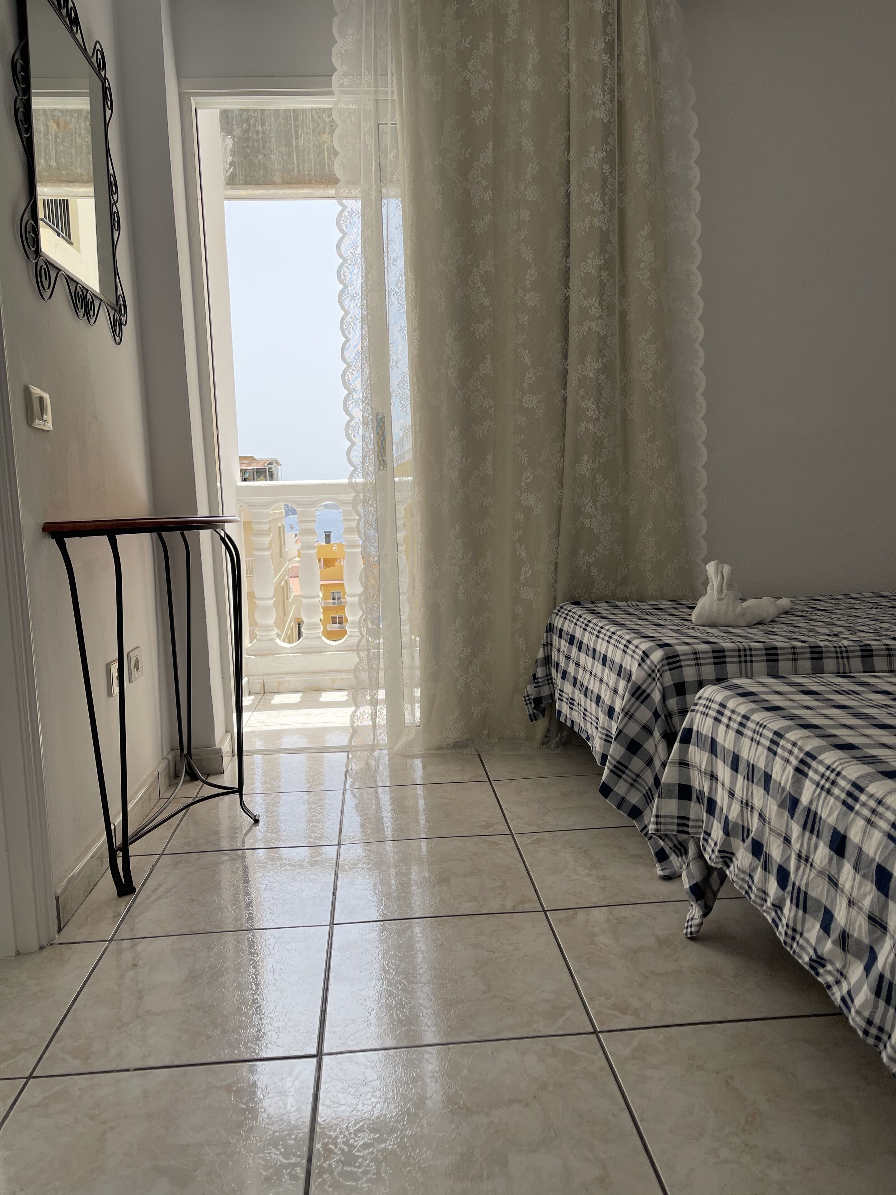 Ein Zimmer mit zwei Betten, einem Balkon, einem dekorativen Spiegel und Blick auf Gebäude.
