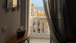 Quarto com varanda, uma mesa com cesta, um espelho e vista para edifícios e mar.