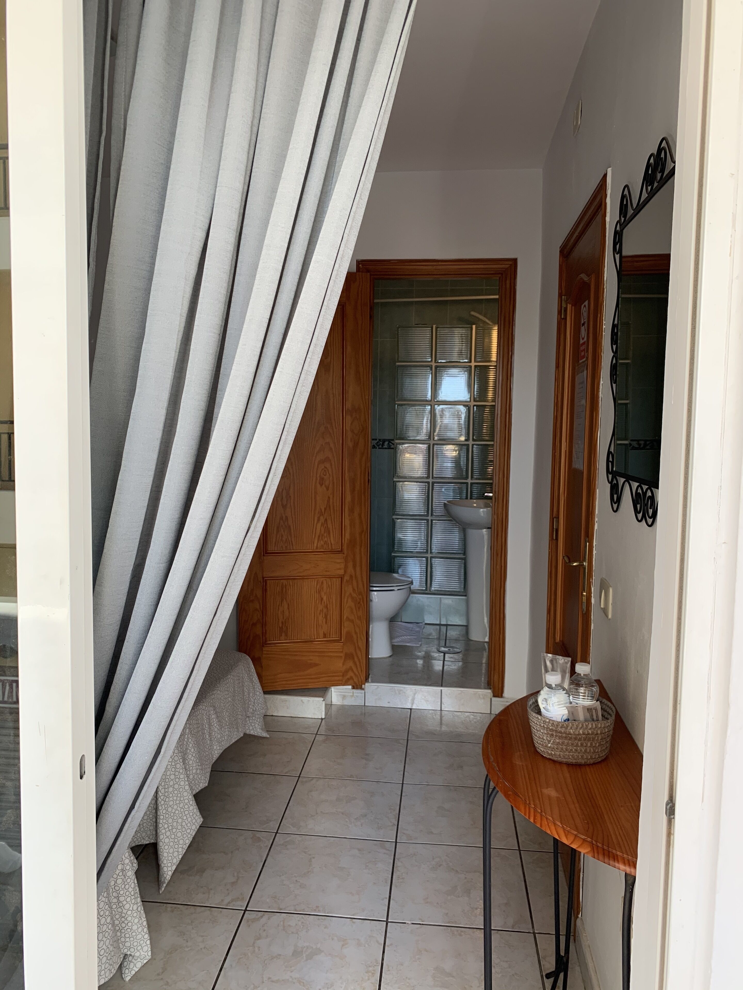 A hallway with a tiled floor, a wooden door, a small table with a basket, and a curtain partially drawn.