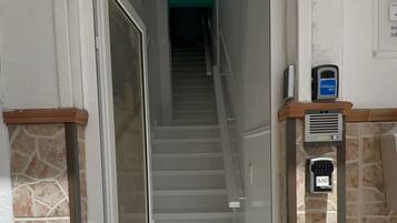 Entrada de hotel con puerta de vidrio, escalera que lleva al piso superior y un teclado de seguridad en la pared.