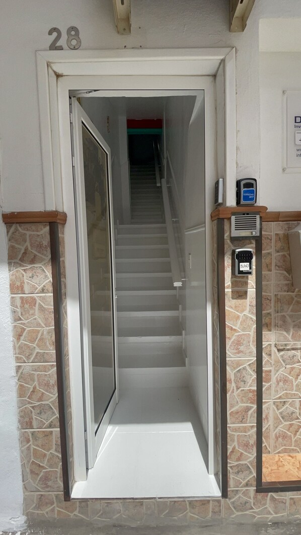 A hotel entrance with a glass door, a staircase leading to the upper floor, and a security keypad on the wall. - Pension Casa Blanca (Arona)