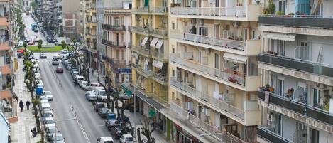 Un edificio de varios pisos con balcones, coches aparcados y una acera.