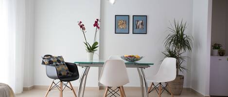 A modern dining area with a glass table, white chairs, and a potted plant.