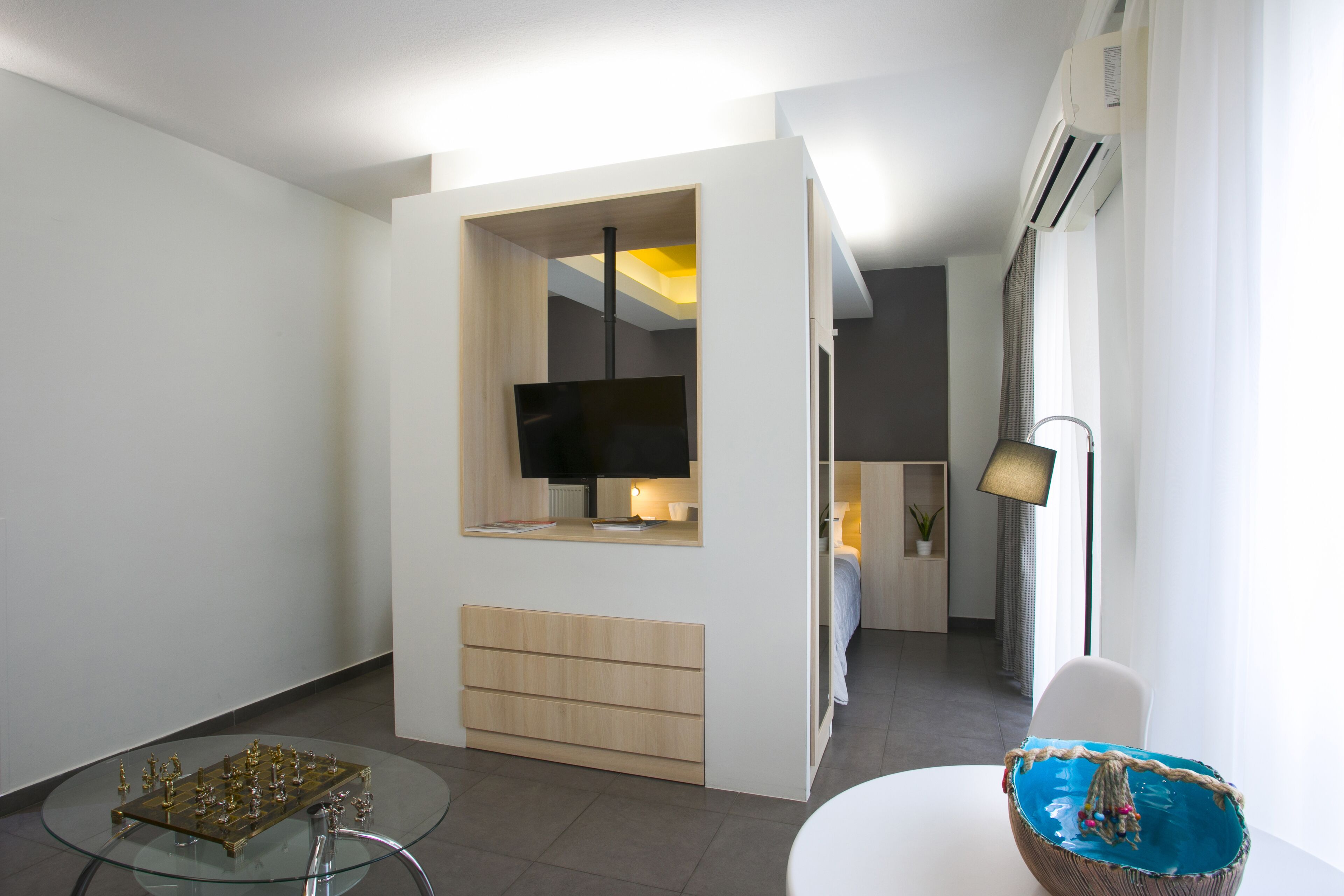 Ein modernes Wohnzimmer mit einem Glastisch, einem Wand-Fernseher, einer Couch und einem Esstisch mit einer dekorativen Schale.