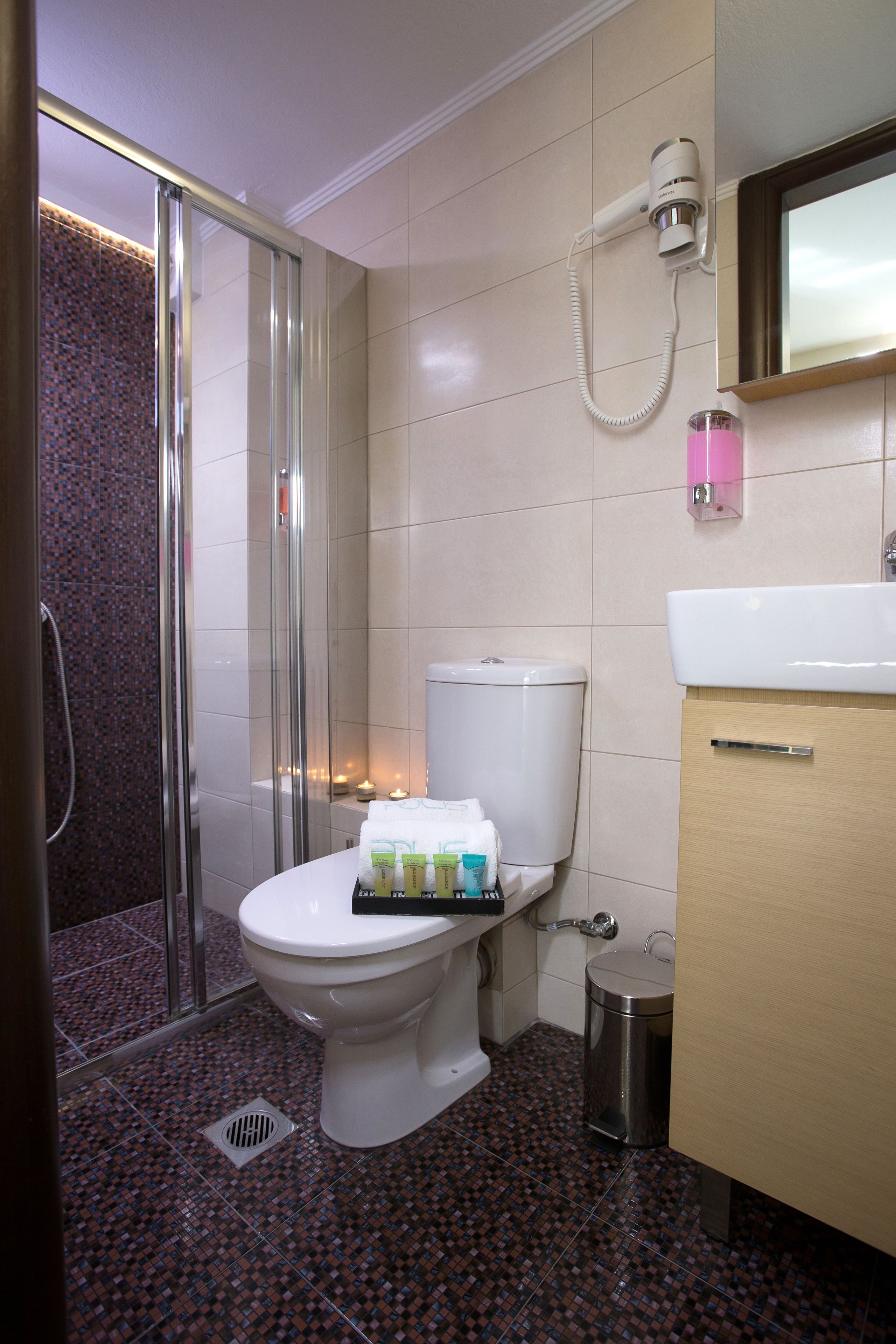 A bathroom with a glass shower enclosure, a toilet, a sink, and a trash can.
