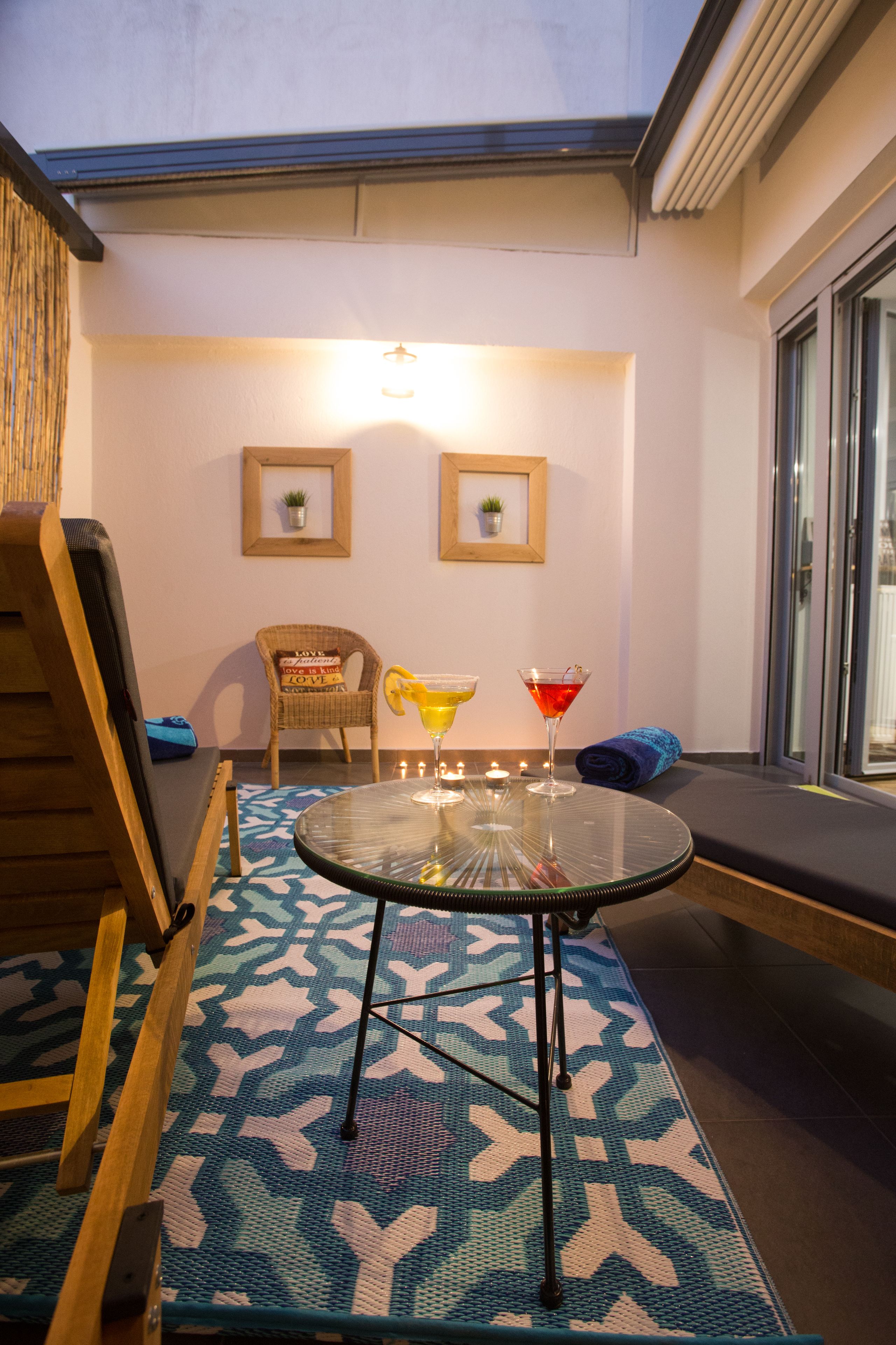 A cozy seating area with a round glass table, two wicker chairs, and a blue patterned rug.