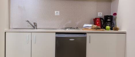 A compact kitchen with white cabinets, a stainless steel dishwasher, and a countertop with a coffee maker, toaster, and a small plant.