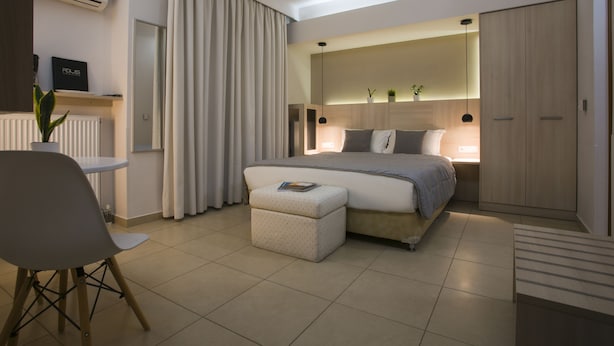 A modern bedroom with a bed, bedside table, chair, and a small table with a plant. - Polis Apartments (Thessaloniki)
