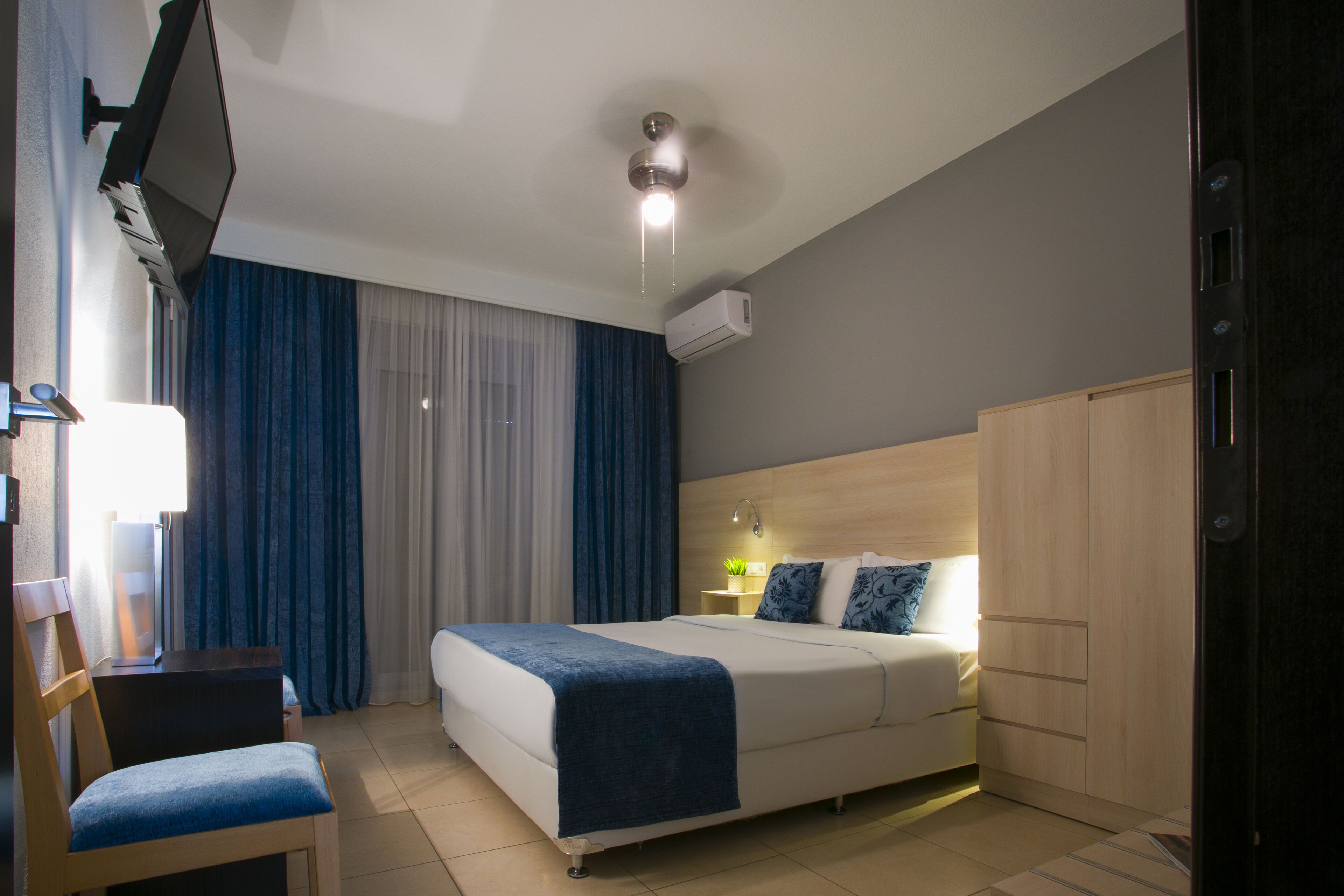 Een hotelkamer met een bed, een bureau met stoel, een kledingkast en een plafondventilator.