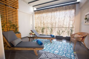 A sunlit room with two lounge chairs, a small table with a drink, and a wicker chair.