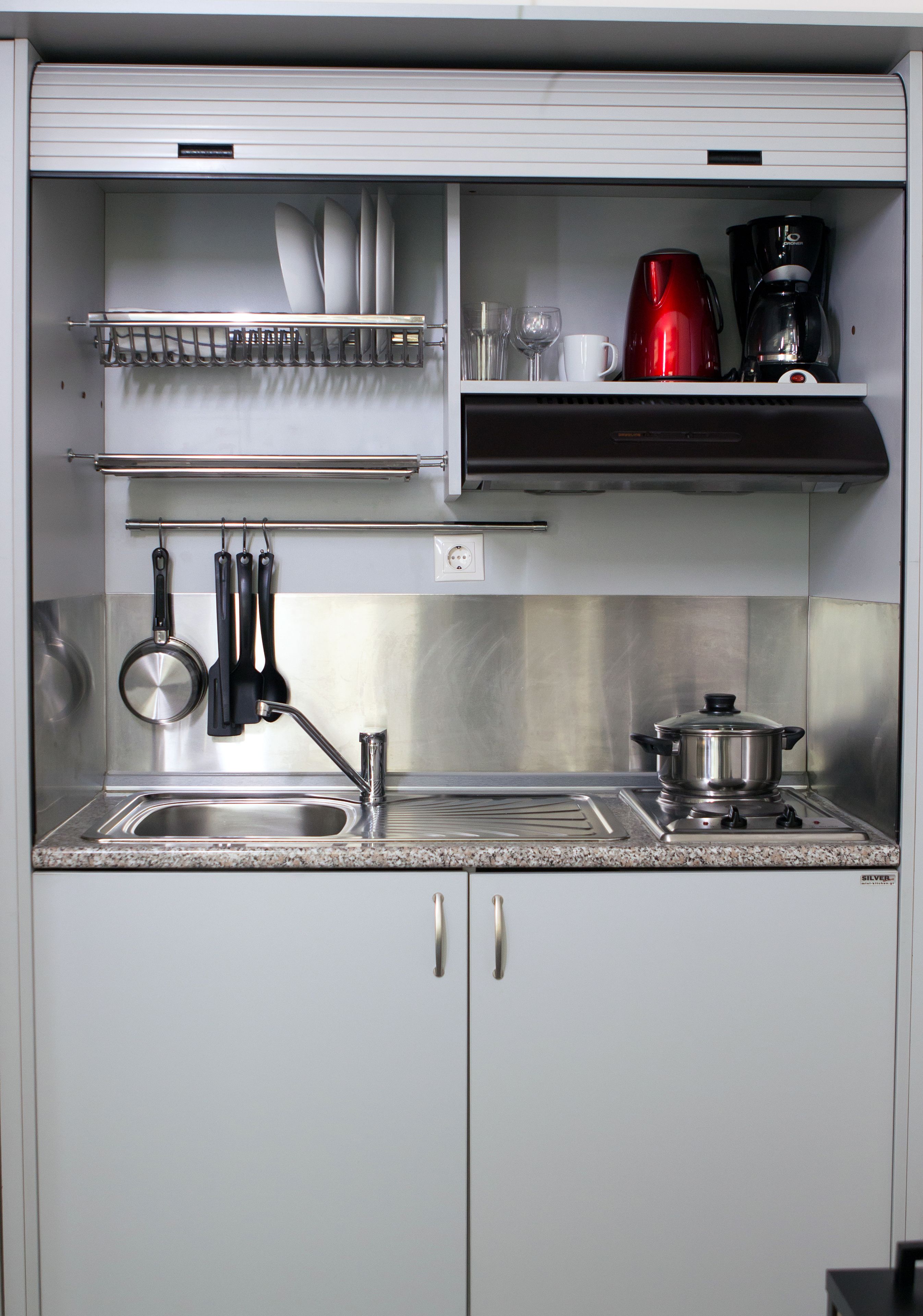 Une cuisine avec un évier en acier inoxydable, une casserole sur la cuisinière et des ustensiles de cuisine accrochés au mur.