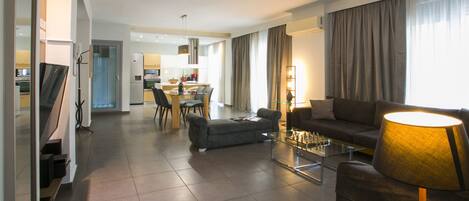 A modern living room with a sofa, a coffee table, and a lamp. There is a dining area in the background with chairs and a table.