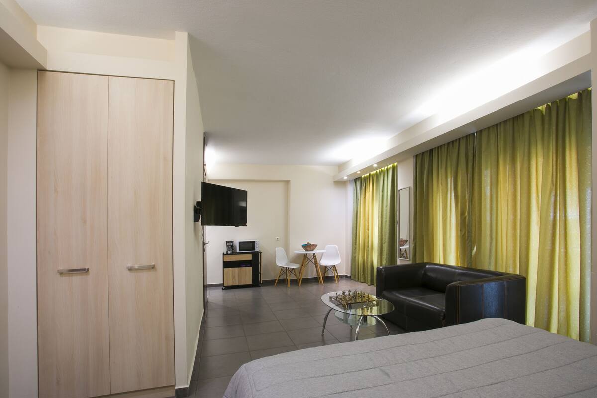 A hotel room with a bed, a desk, a chair, a sofa, and a dining area with a table and chairs.