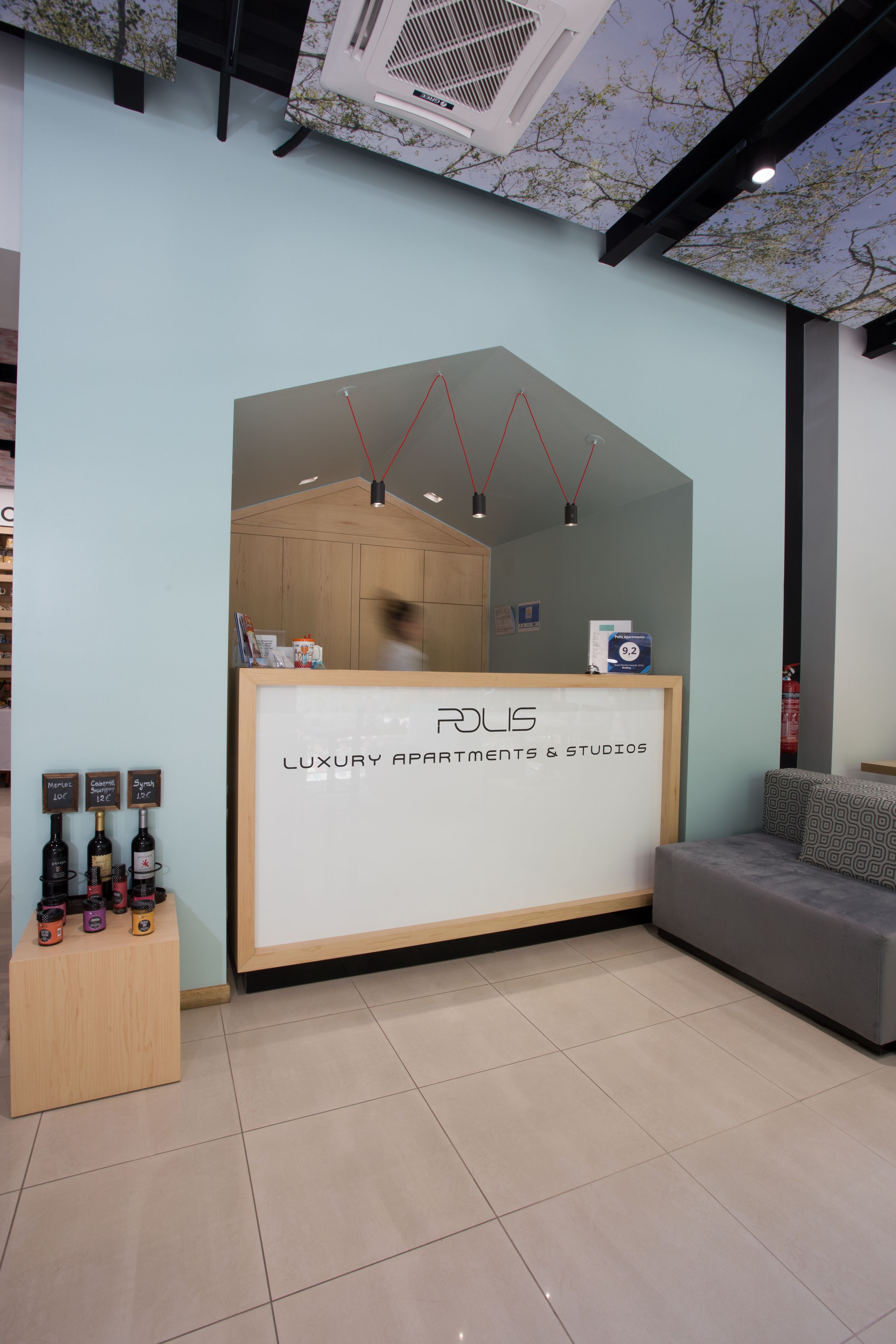 A reception area with a sign reading "Rolis Luxury Apartments & Studios," a wooden counter, and a display of wine bottles.