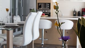 A modern kitchen with white bar stools, a dining table, and a vase with flowers. - Polis Apartments (Thessaloniki)