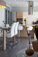 A modern kitchen with white bar stools, a dining table, and a vase with flowers.