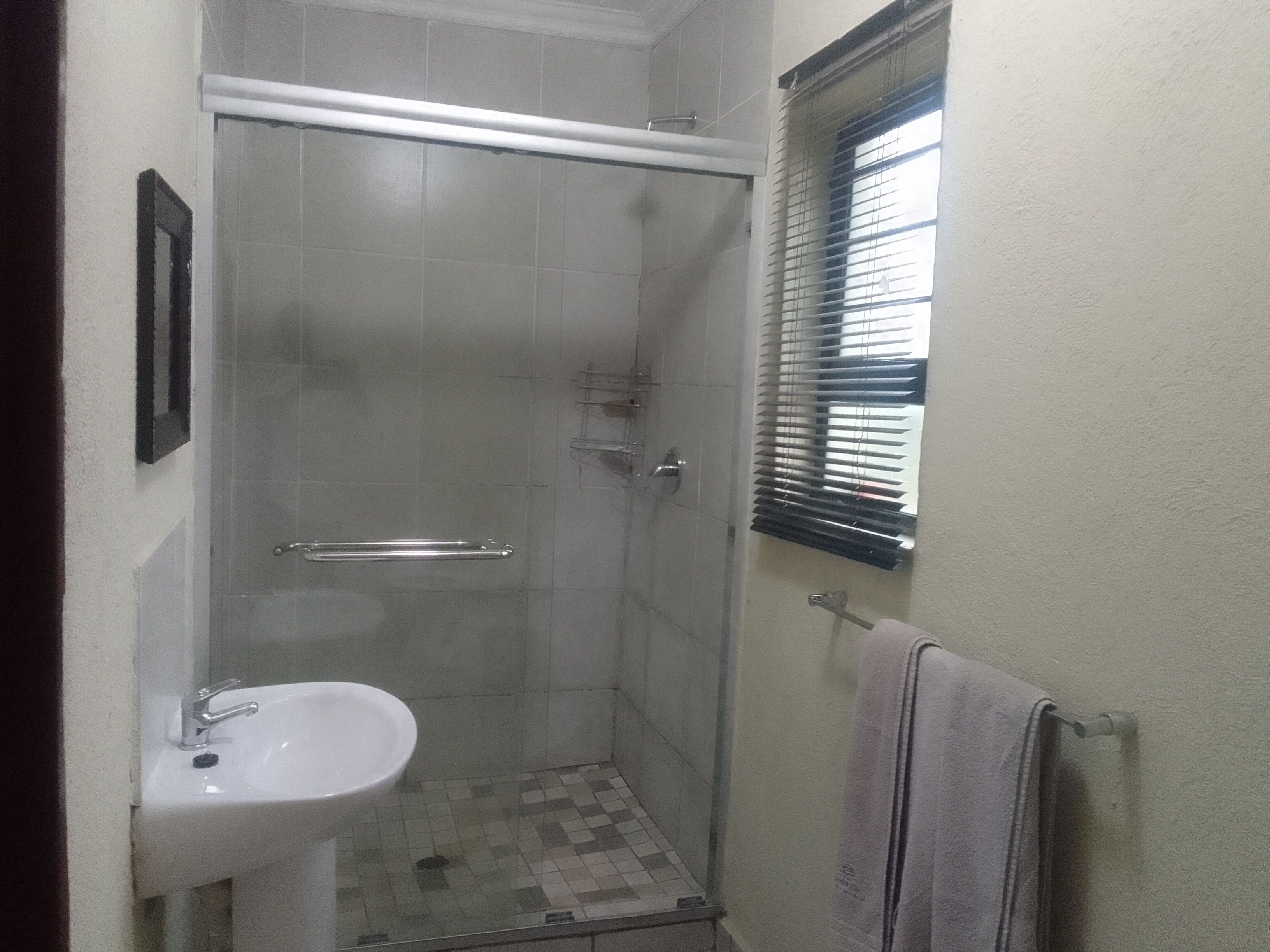 Un baño pequeño con ducha, lavamanos y una ventana con persianas.