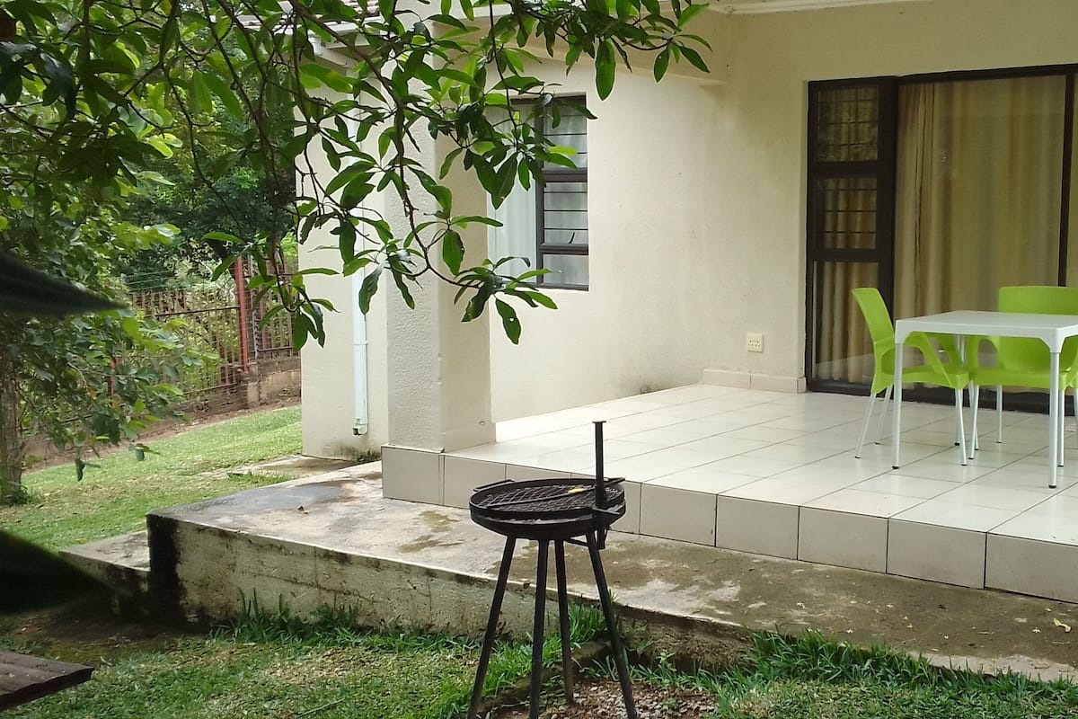 A patio area with a small table and chairs, a concrete ledge, and a view of a building through a window.