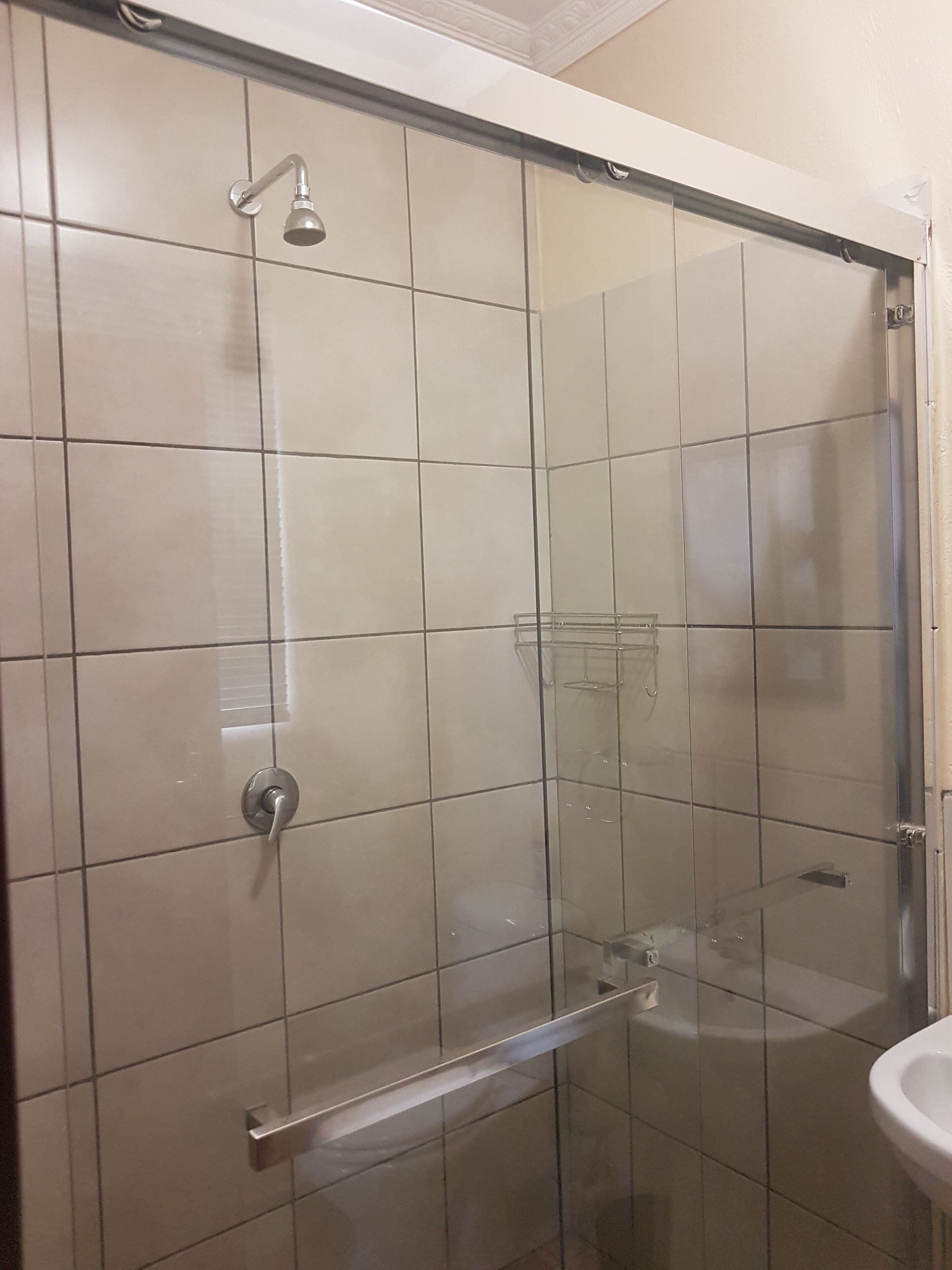A glass-enclosed shower with a handheld showerhead and a glass shelf.