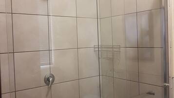 A glass-enclosed shower with a handheld showerhead and a glass shelf.