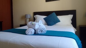 Un lit bien fait, avec du linge de lit blanc, un plaid turquoise et des serviettes enroulées posées sur le bord. Un oreiller bleu est placé sur le lit.