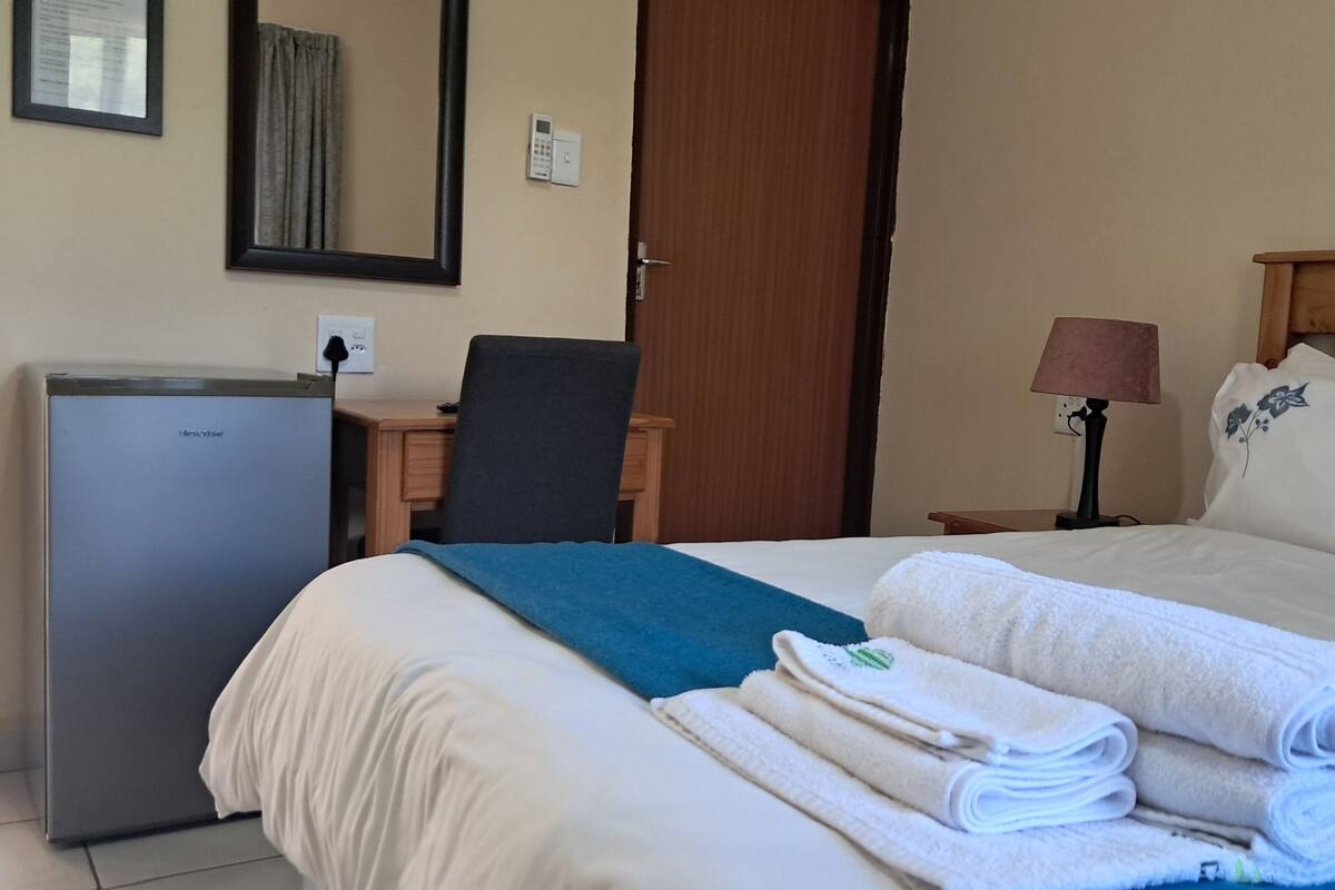 A hotel room with a bed, a desk, a chair, a lamp, a wardrobe, and a refrigerator.