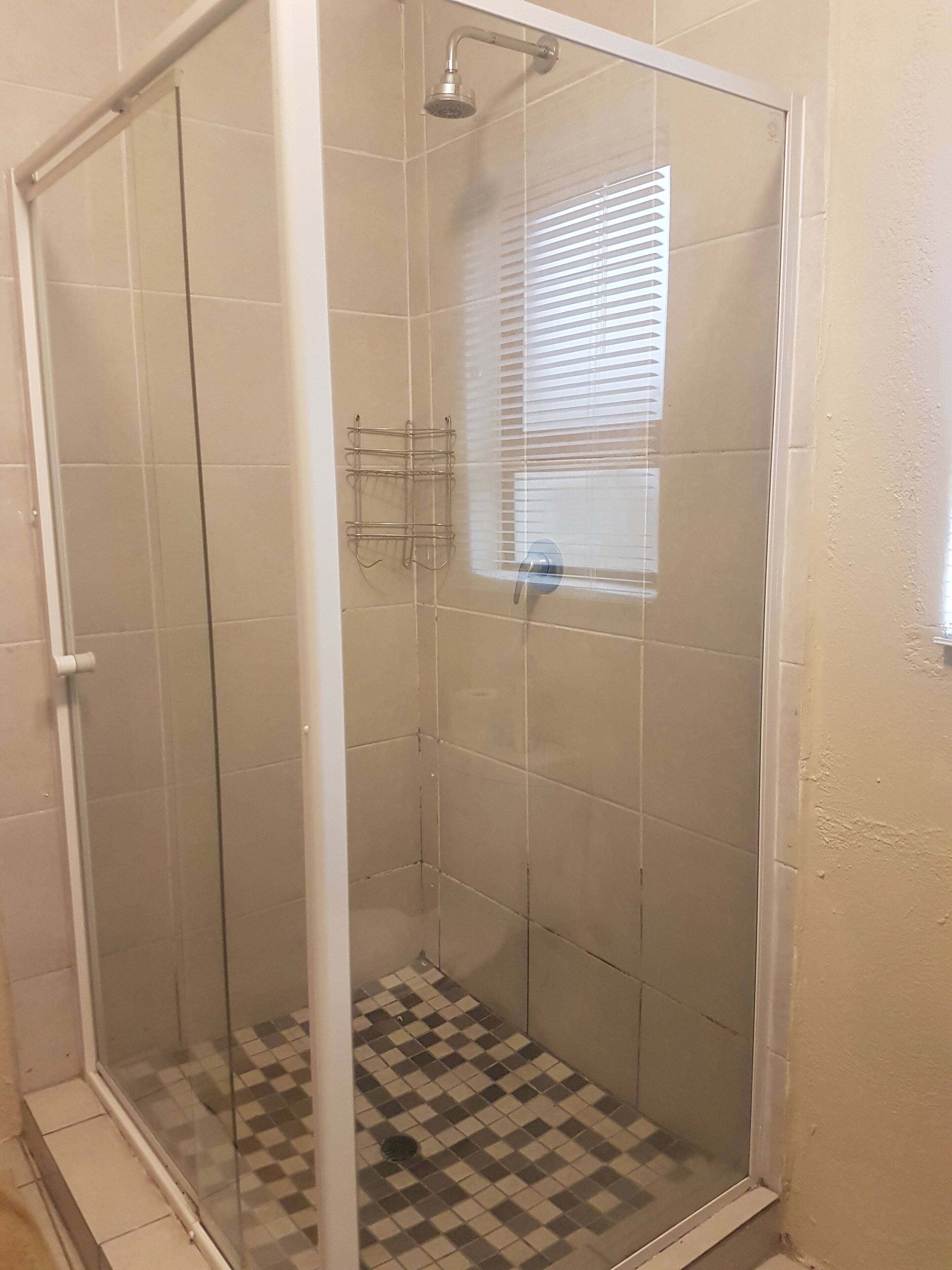 A glass-enclosed shower with a checkered floor, a window with blinds, and a towel rack.