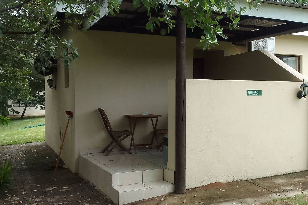 A covered outdoor seating area with a 'WEST' sign, a small table, and a chair.