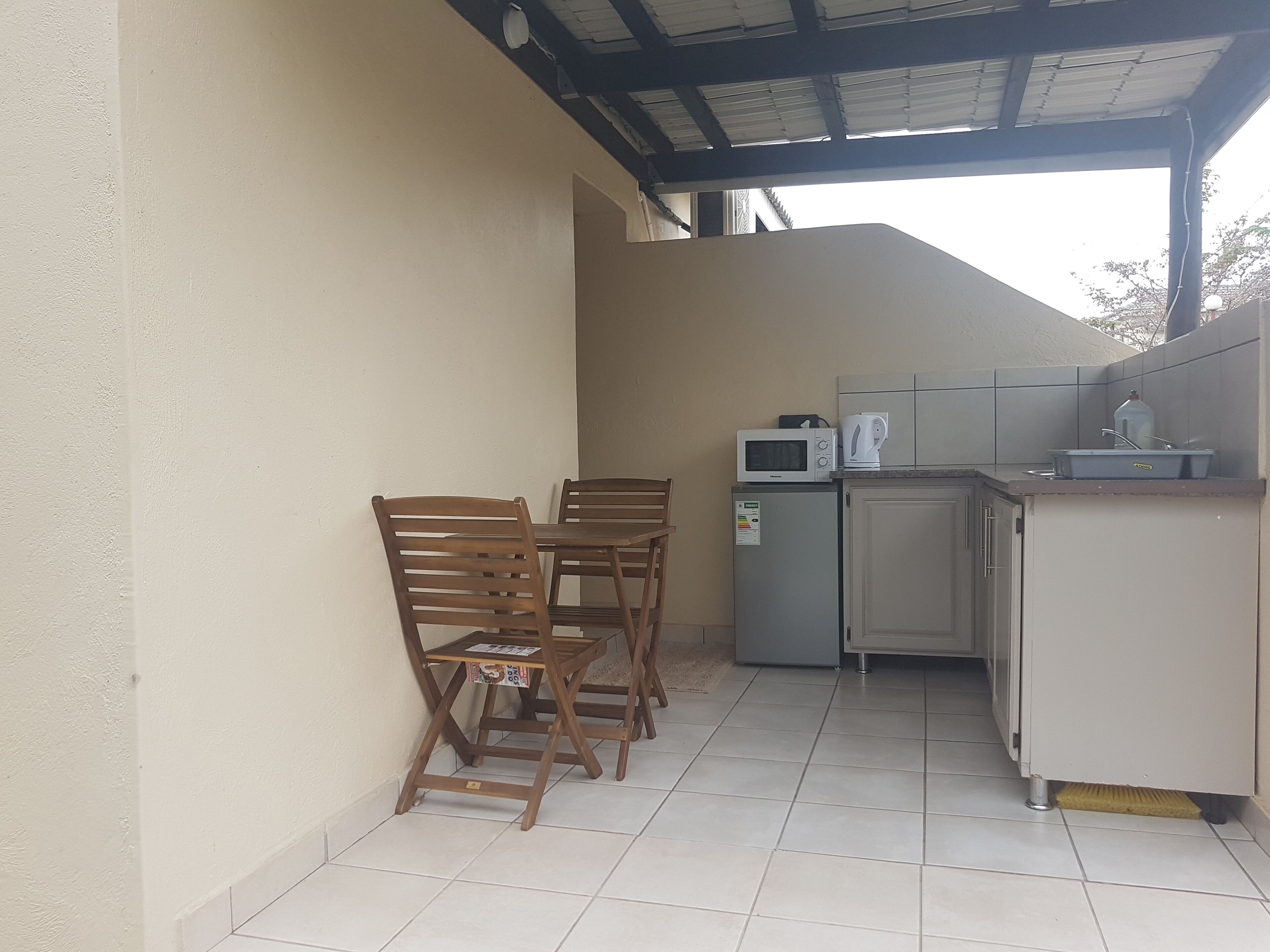 A small kitchenette with a microwave, kettle, and sink. There are two wooden chairs and a small table.