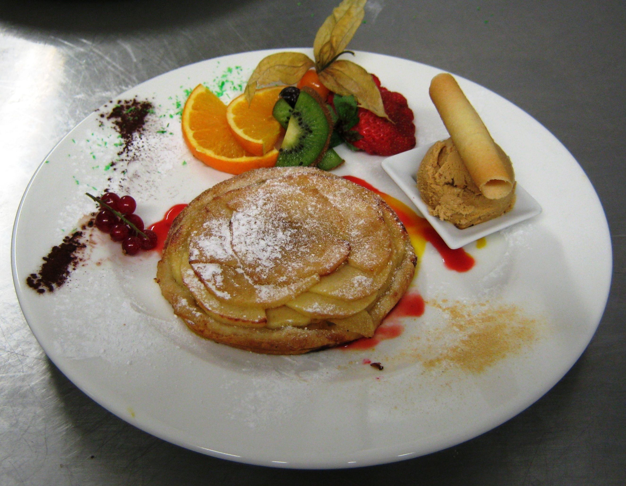 Une assiette avec des crêpes, des fraises, des kiwis, des tranches d’orange et une petite pâtisserie.
