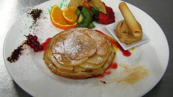 Une assiette avec des crêpes, des fraises, des kiwis, des tranches d’orange et une petite pâtisserie.