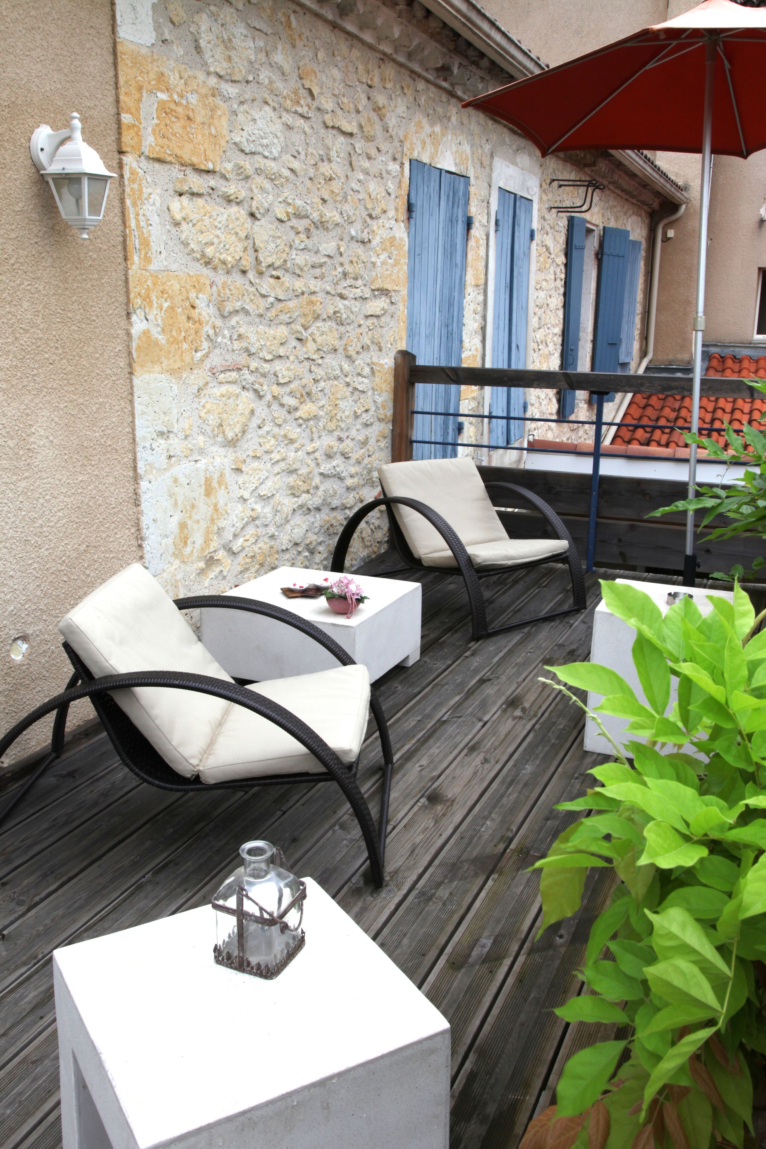 Une terrasse en bois avec deux chaises blanches rembourrées, une petite table et un pot de fleurs.