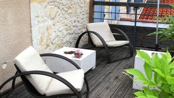 Une terrasse en bois avec deux chaises blanches rembourrées, une petite table et un pot de fleurs.