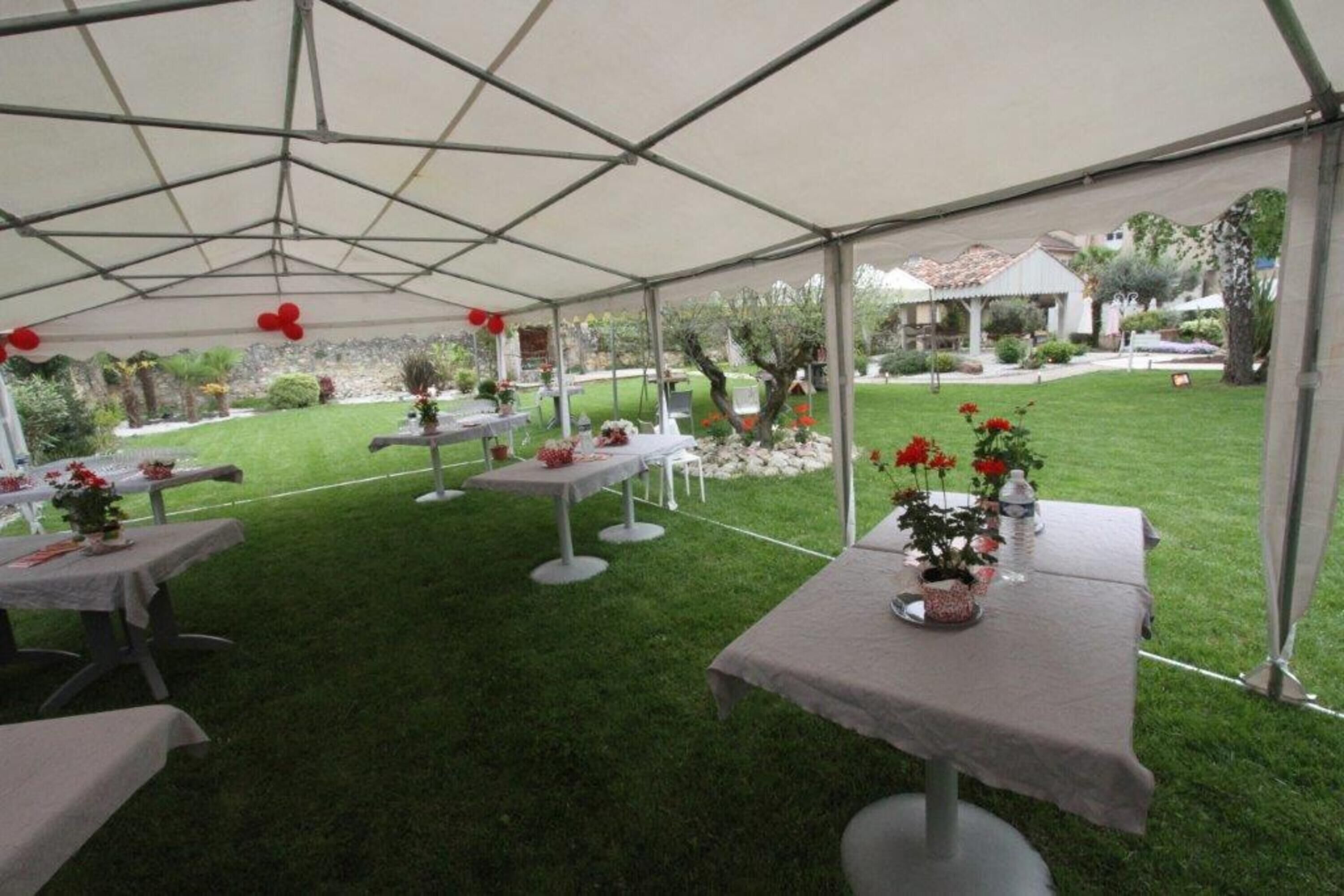 Tienda de campaña al aire libre con mesas dispuestas para comer, rodeada de césped y jardín bien cuidados.