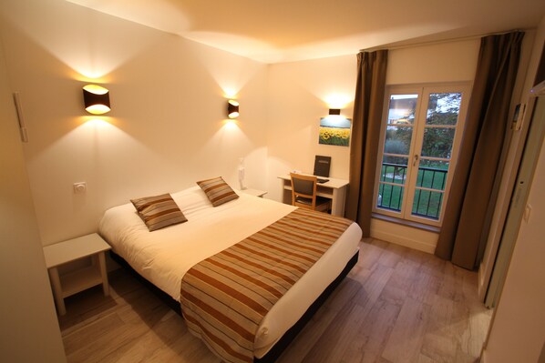 A bedroom with a bed, bedside tables, a desk, and a window with curtains.